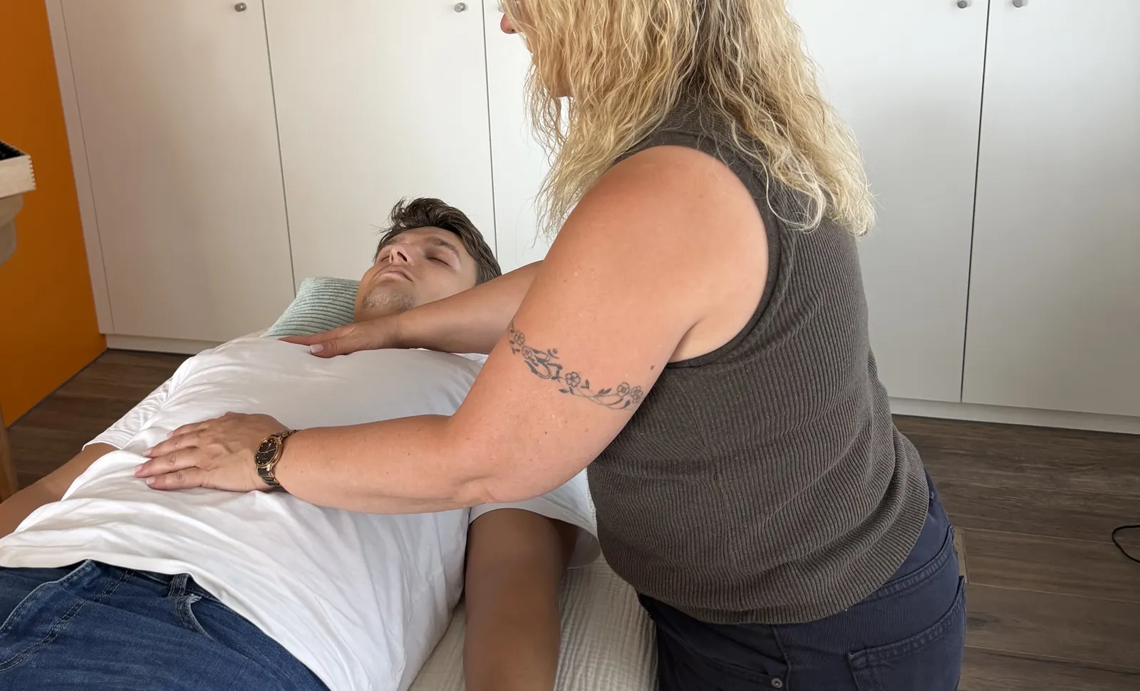 Mariana legt einer angezogen auf der Liege ruhenden Person die Hände auf Brust und Bauch.